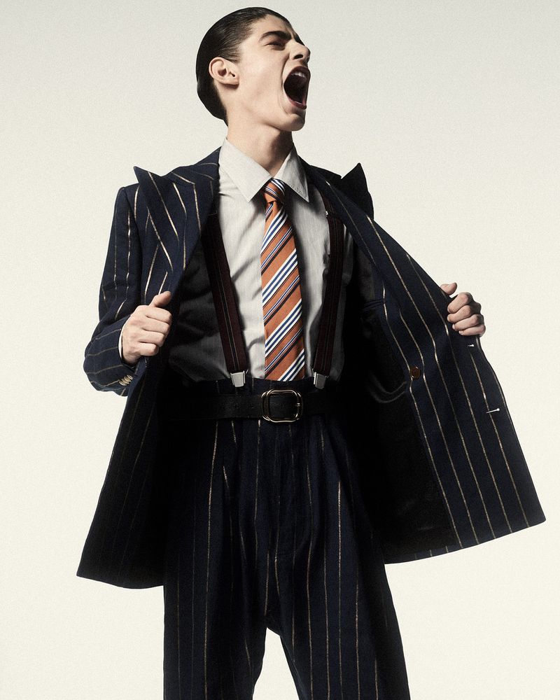Model Baptiste Vivo shouting while wearing a pinstripe suit with suspenders and a striped tie against a white background.