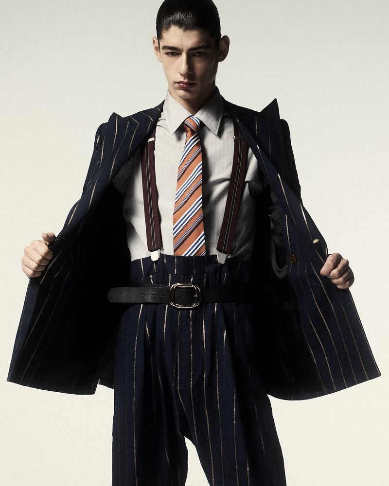 Model Baptiste Vivo posing in an open pinstripe suit, striped necktie, and suspenders against a light studio backdrop.