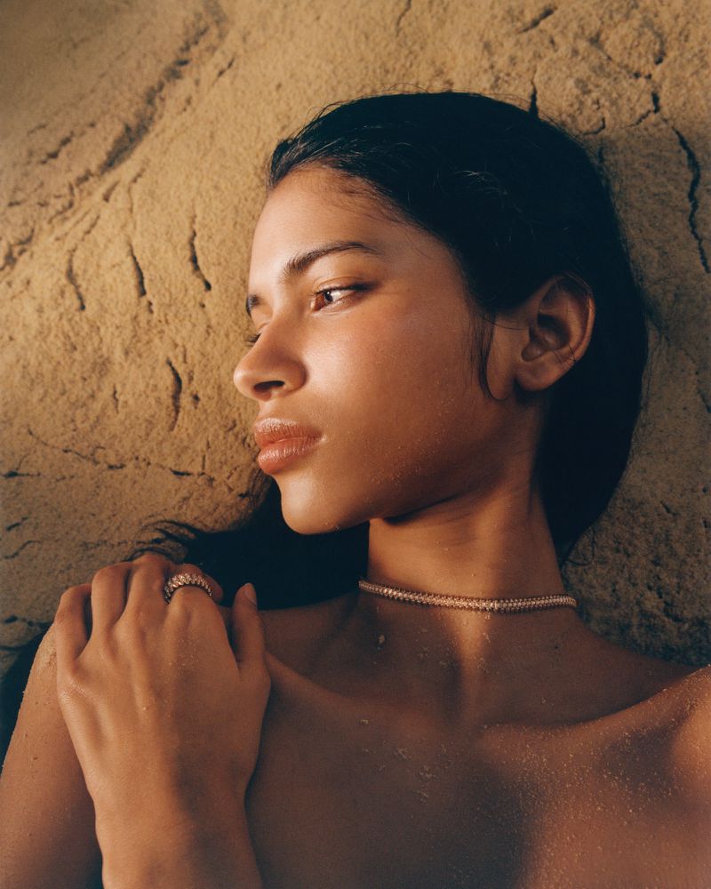 Close-up portrait of Liseth Sairys wearing a choker necklace and ring against a textured sand backdrop for Harper's Bazaar France.