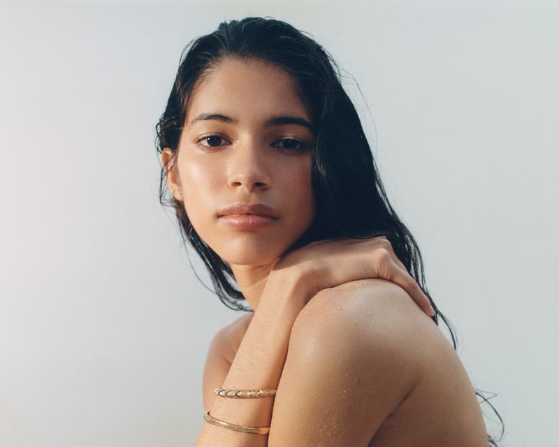 Liseth Sairys with wet hair and bare shoulders wearing gold bracelets against a white background for Harper's Bazaar France.