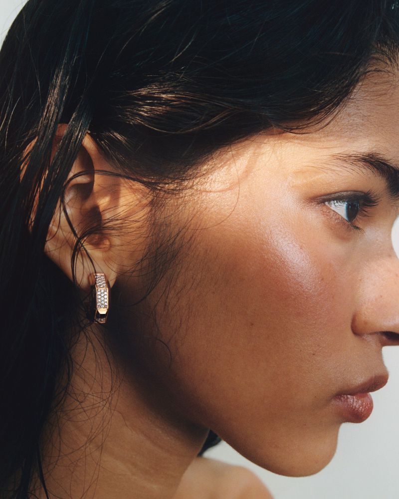 Close-up portrait of a woman wearing a diamond pave hoop earring with warm sunlight casting light across her face.