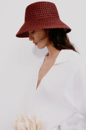 Model wearing a brown crochet bucket hat and white shirt against a seamless white background for H&M.