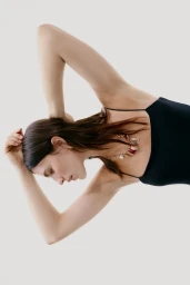 Model in a black spaghetti strap top wearing a gold statement necklace against a plain white background