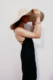Model wearing a wide-brimmed straw hat and a black slip dress against a white background for H and M