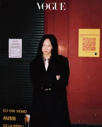 Model Yun Seo Woo posing in a black tailored coat outside a Parisian storefront with French signage for Vogue Korea.
