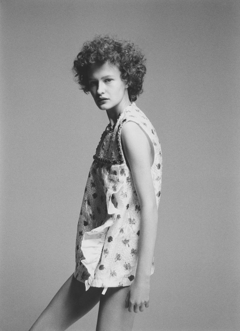 Model Kris Krystal posing in a patterned sleeveless ruffled top against a plain neutral studio background.