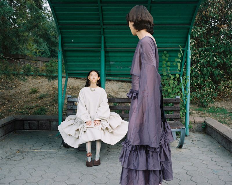 Fashion models in voluminous ruffled dresses posing at a green outdoor shelter for Vogue Czechoslovakia.