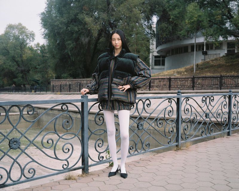 Model Aldiyar Amangeldy posing by a decorative iron railing in a striped quilted vest and white tights for Vogue Czechoslovakia.