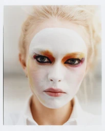 Close-up beauty portrait of model Yana Palkhouskaya wearing theatrical white face paint and colorful eye makeup with a white shirt.