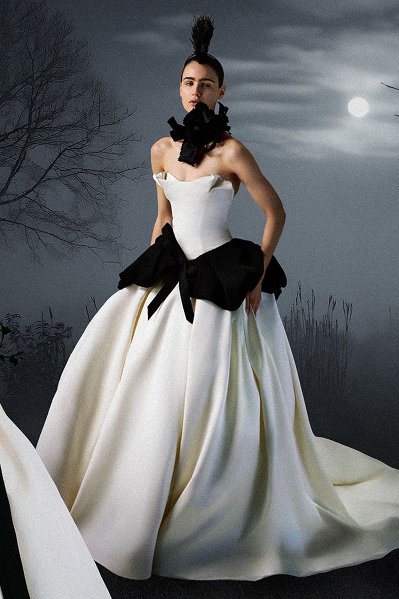 A woman wears a dramatic white ballgown with a black ribbon detail in a misty outdoor setting, illuminated by moonlight.