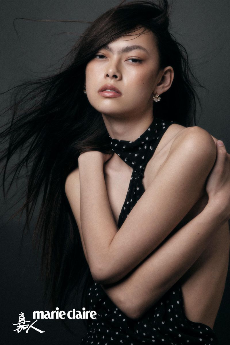 Model with windswept dark hair wearing a black and white polka dot halter garment against a dark studio background.