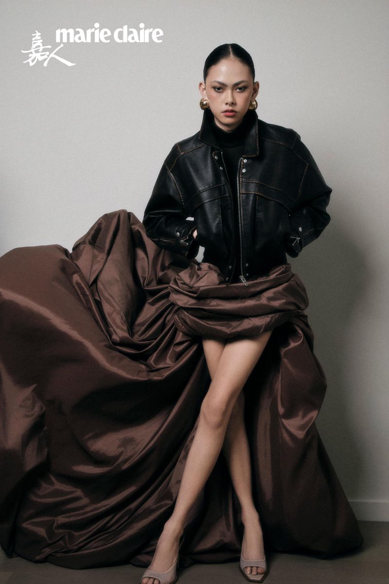 East Asian model wearing a black leather jacket and a voluminous brown satin skirt in a studio fashion editorial.