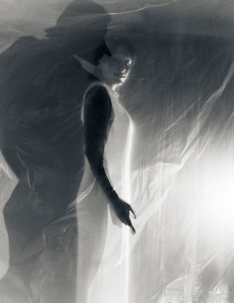 Mason Alexander Park standing behind translucent draped plastic sheet with high-contrast lighting and shadows.