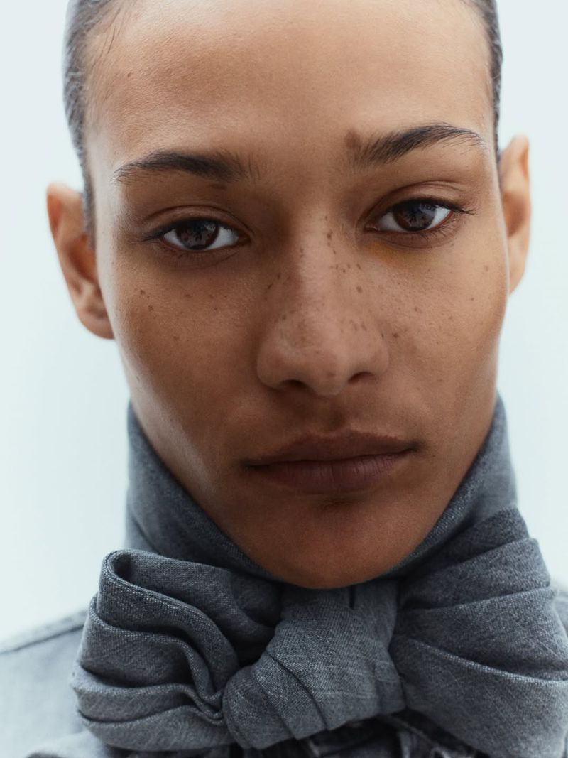 Close-up portrait of model Mar G wearing a tied grey textured fabric neck scarf against a pale backdrop.