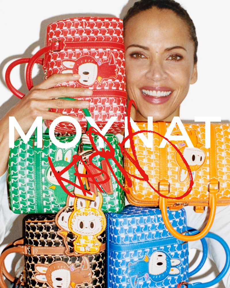 Smiling woman poses behind a stack of five patterned Moynat handbags in red, green, black, orange, and blue, against a white backdrop.