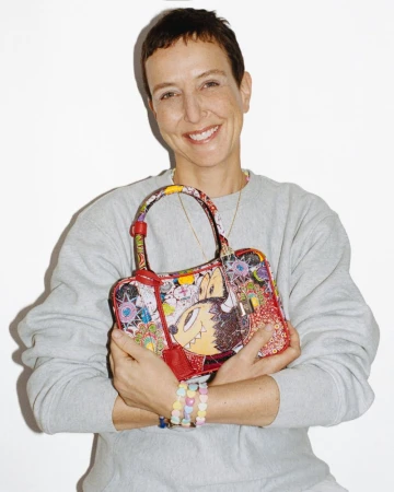 Smiling woman holding a brightly patterned handbag wearing a grey sweatshirt against a plain white background