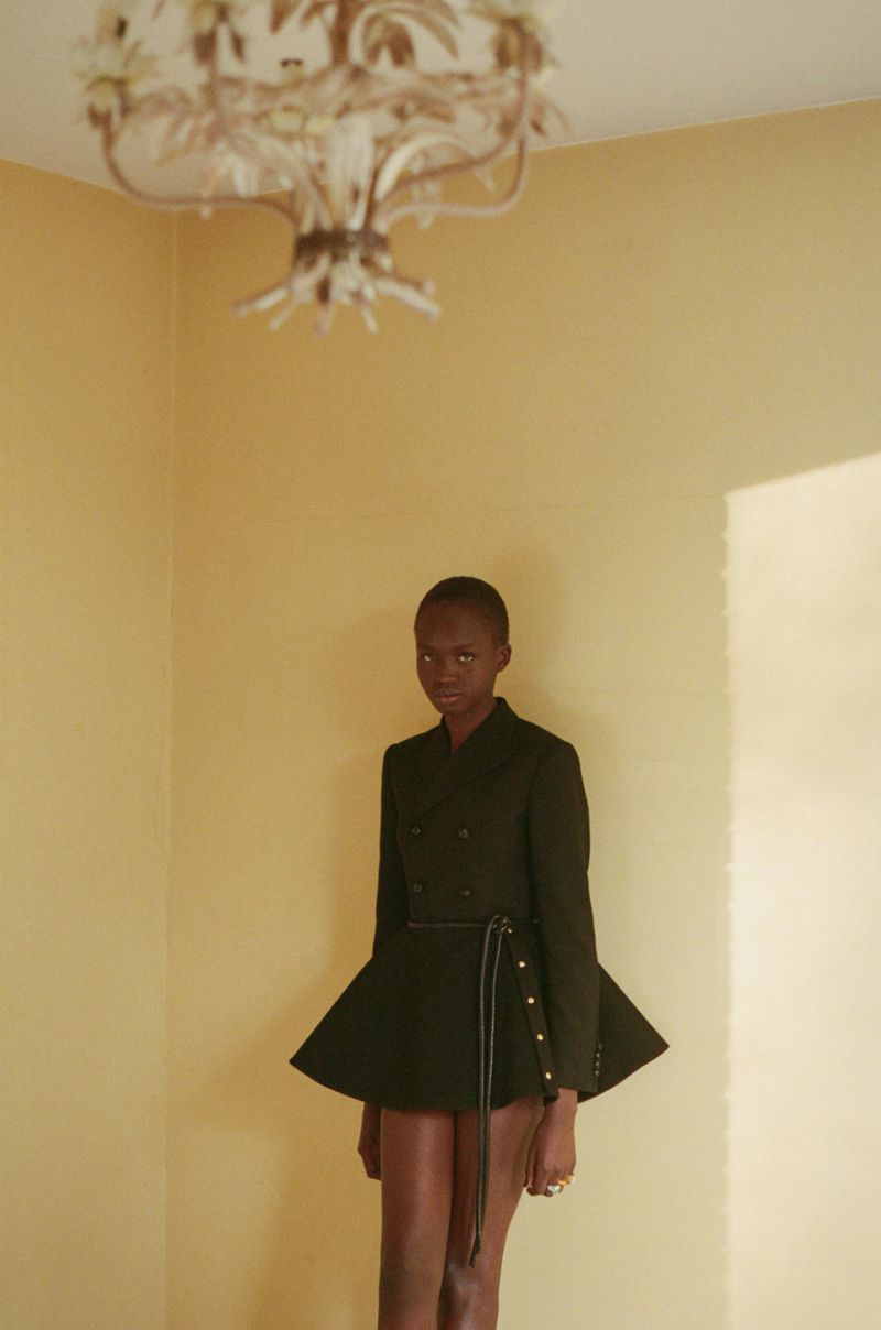 Model Anyier Anei wearing a structured black jacket in an interior with a vintage chandelier for Russh magazine