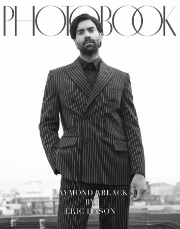 Man wearing a striped double-breasted suit standing against a rooftop background for Photobook Magazine