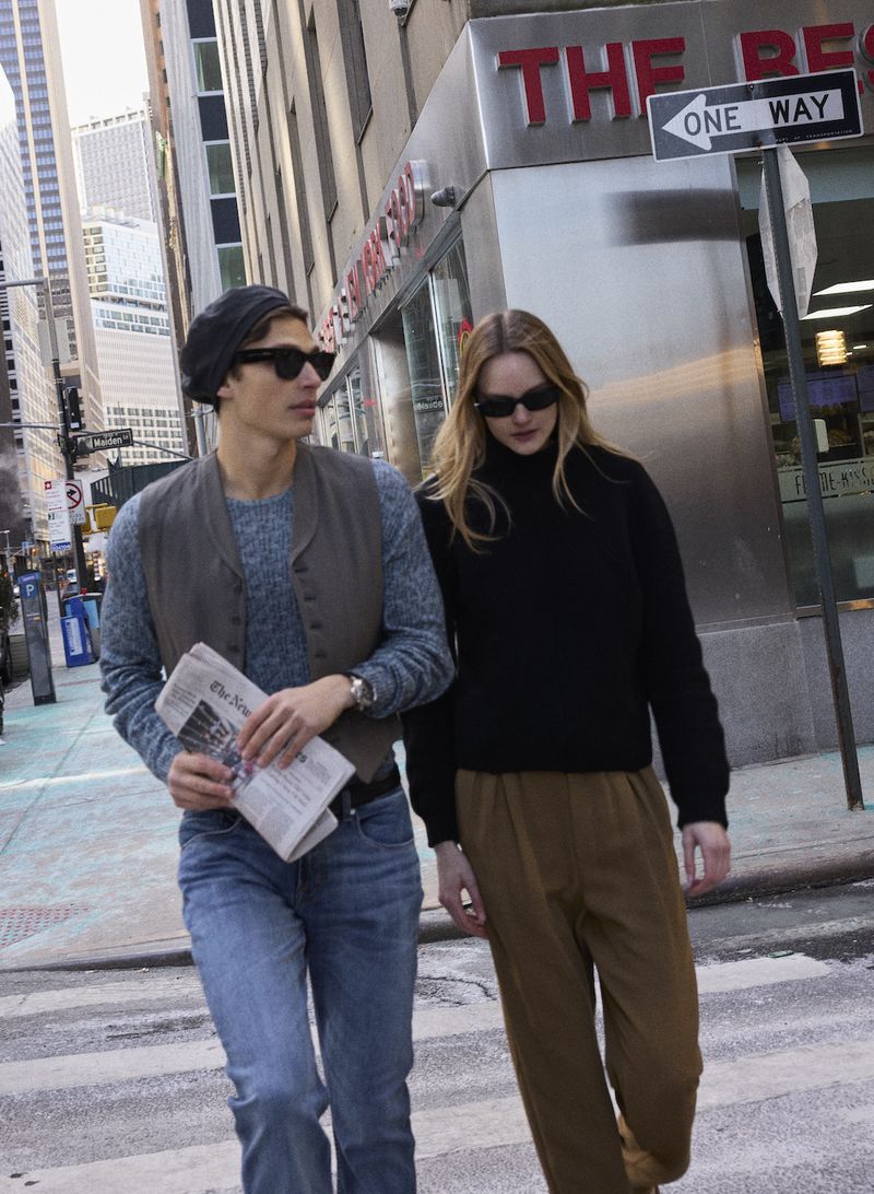 A man and woman walking down a city street wearing sunglasses, knit sweaters, trousers, and a beret.