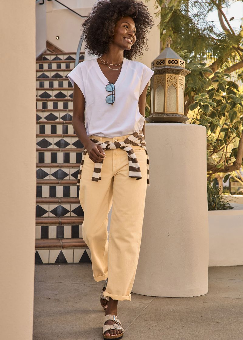 Smiling Black woman walking down stairs wearing a white v-neck t-shirt, pastel yellow cuffed trousers, and buckle sandals.