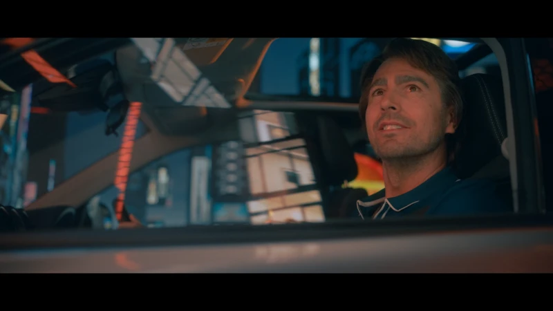 Adult male in a car at night, cityscape background with colorful lights, captured in medium shot showing a contemplative mood.