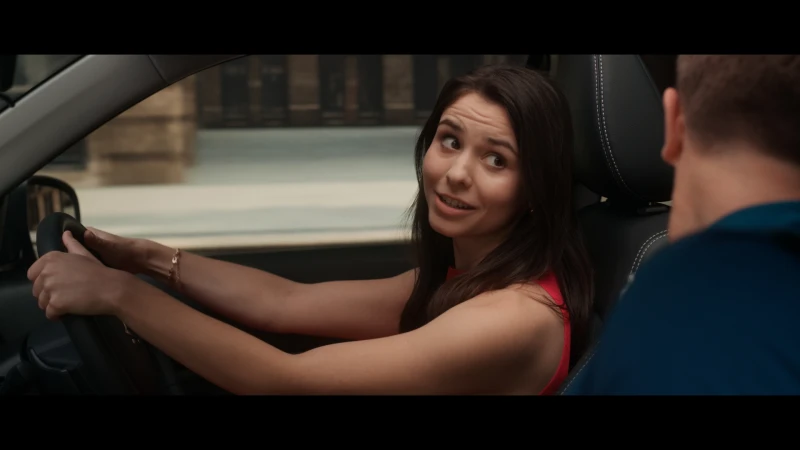 Woman driving a car with a passenger, brunette smiles with hands on the steering wheel, interior shot in natural light.