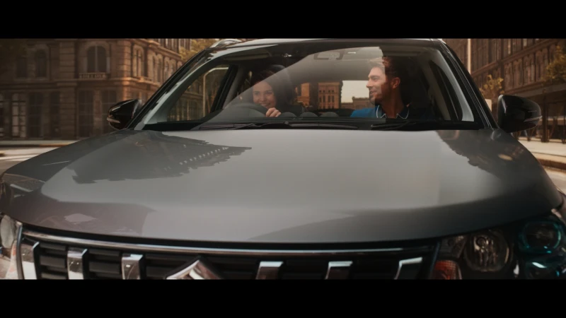 Grey Suzuki SUV driving on a city street with a smiling adult male and female couple visible inside the car.