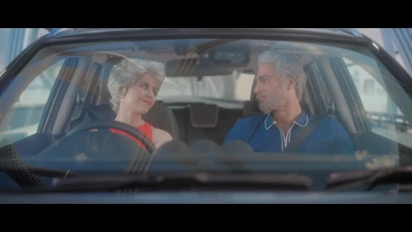 An older man and woman seated inside a car, looking at each other through the windshield during the Suzuki TVC project.