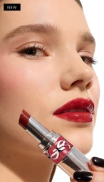 Close-up of a model with glossy red lips holding an open silver lipstick tube against a white seamless background.