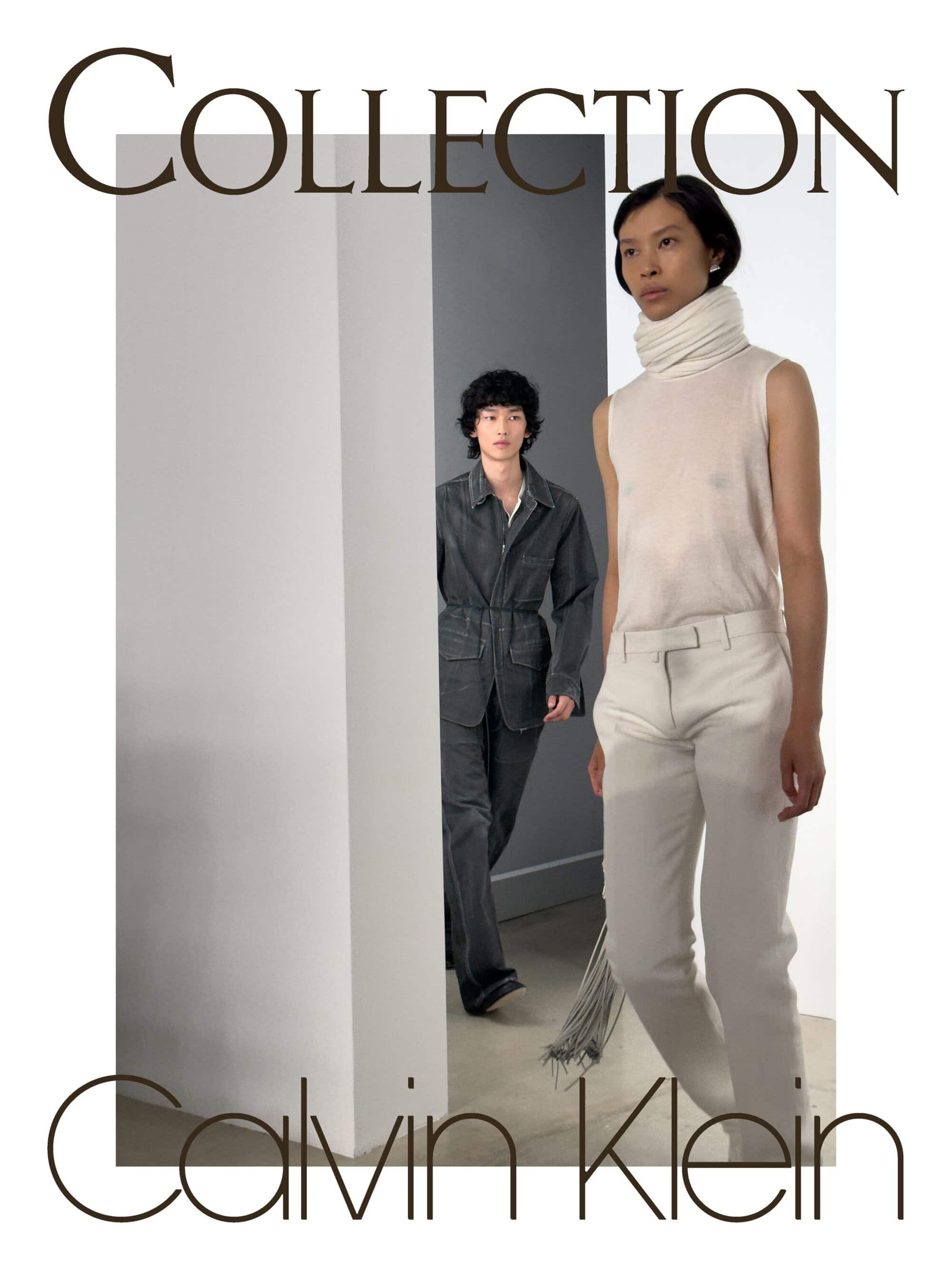 A model in a sleeveless high-neck top and white trousers walks ahead of another model in a charcoal denim suit in a minimalist space.