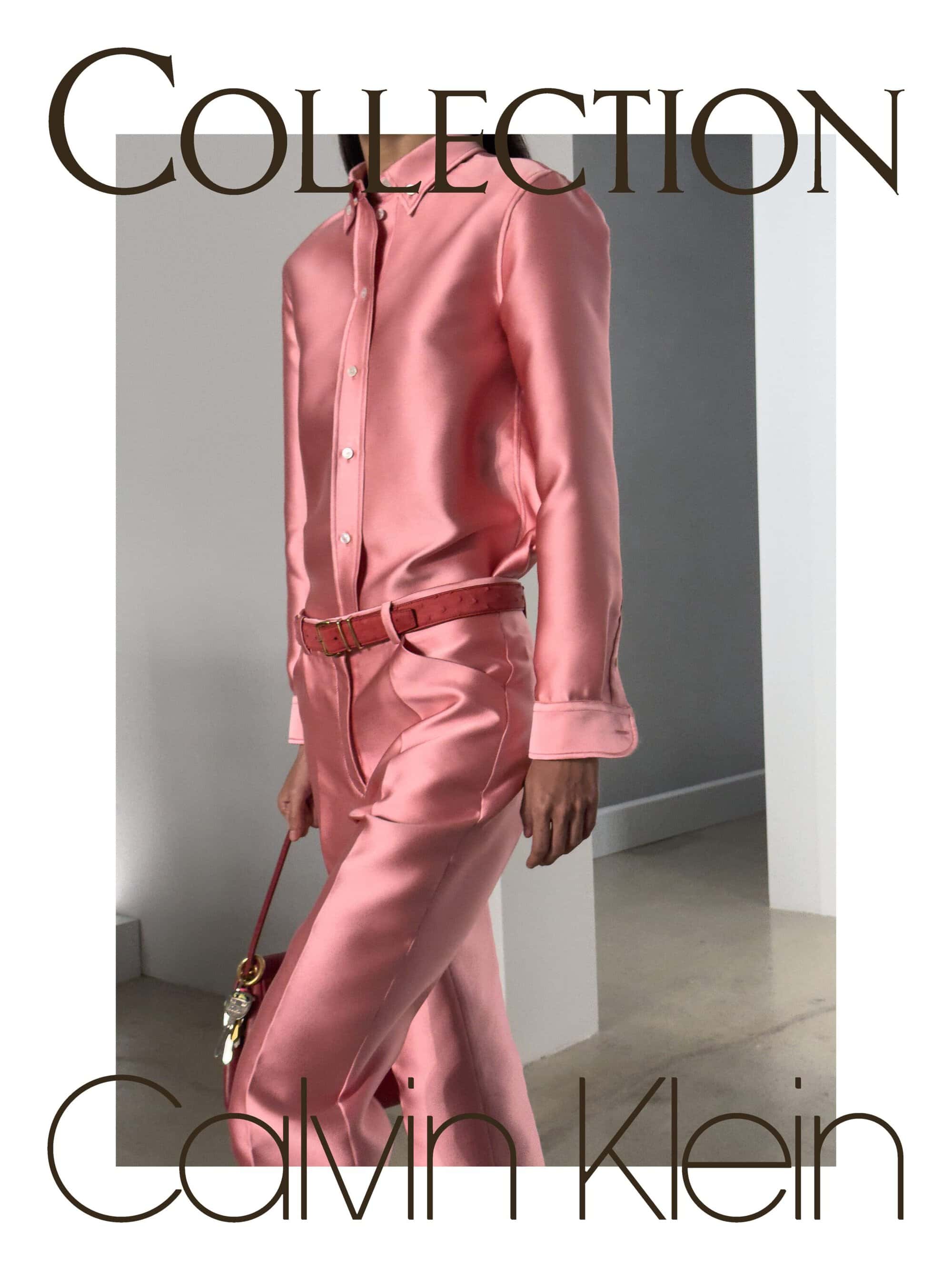 Model wearing a pink satin button-down shirt and matching trousers with a textured belt in a minimalist architectural space.