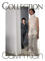 A model in a sleeveless high-neck top and white trousers walks ahead of another model in a charcoal denim suit in a minimalist space.
