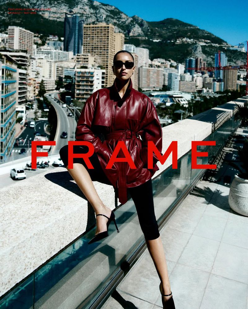Alexandra Leclerc wearing a belted burgundy leather jacket, black sunglasses, and high heels on a rooftop overlooking Monaco.
