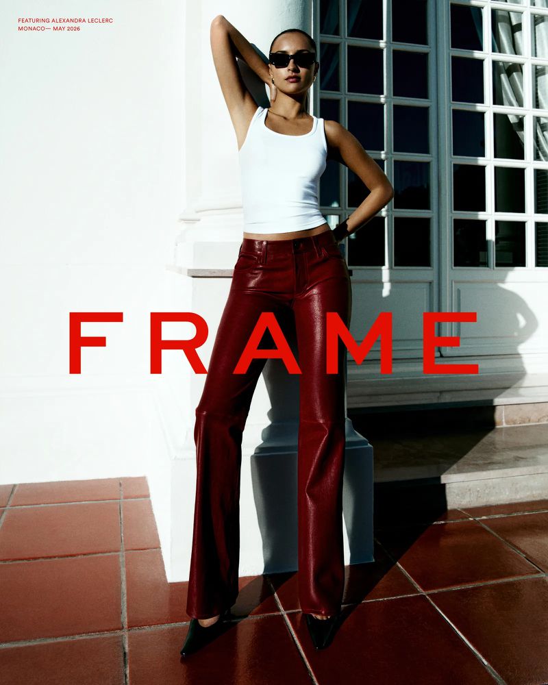 Alexandra Leclerc wearing a white tank top and burgundy leather trousers posing outdoors by a white architectural column for FRAME.