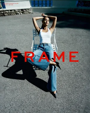 Alexandra Leclerc wearing a white tank top and wide-leg denim jeans seated on a white chair in direct sunlight.