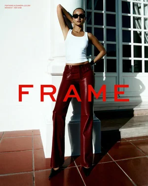 Alexandra Leclerc wearing a white tank top and burgundy leather trousers posing outdoors by a white architectural column for FRAME.