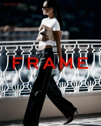 Woman in white t-shirt and black leather pants walking past a white stone balustrade