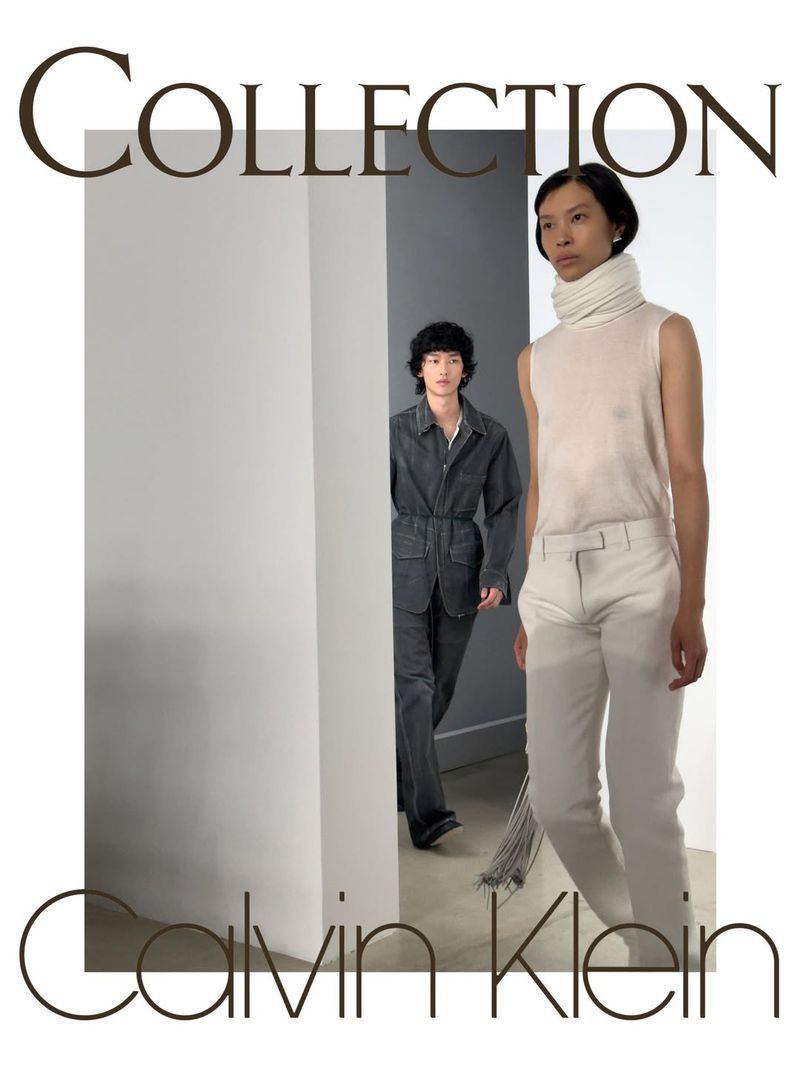 Model wearing a white high-neck sleeveless top and tailored white trousers standing before an interior doorway with another model behind.