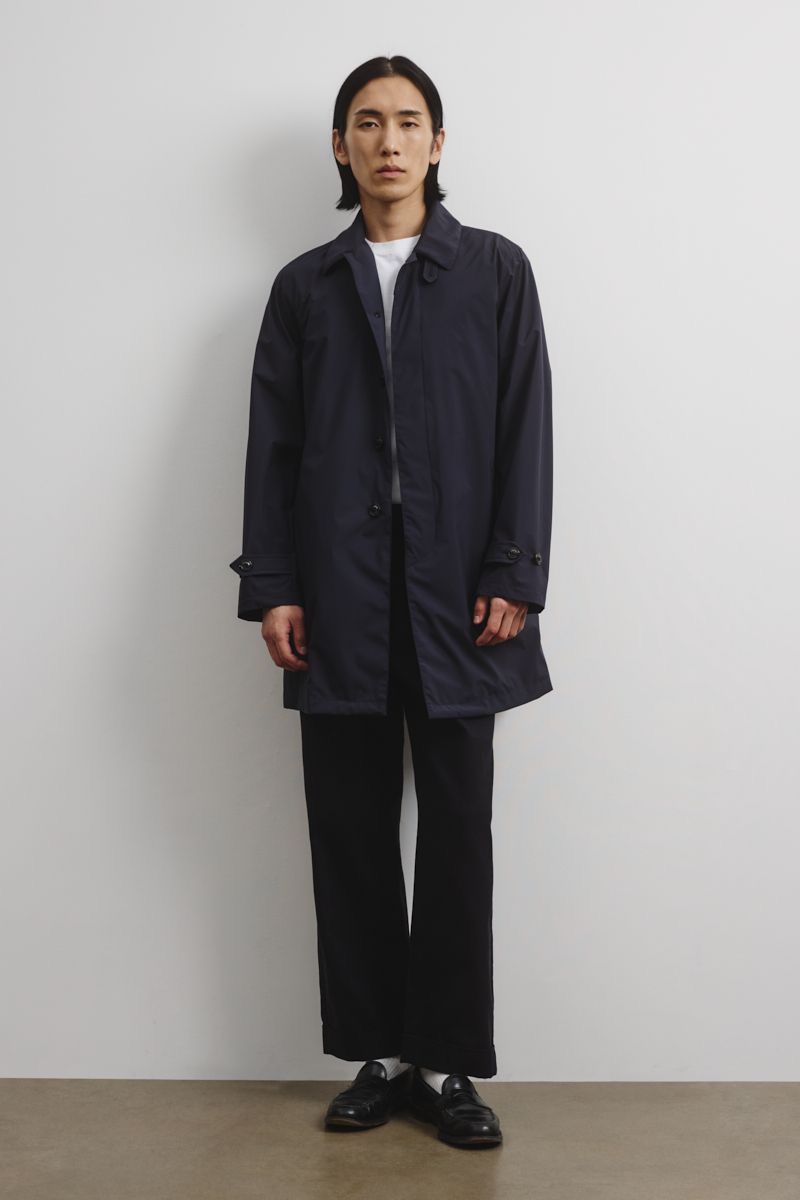Full-length studio shot of an adult male wearing a navy trench coat, black trousers, and dress shoes against a neutral background.