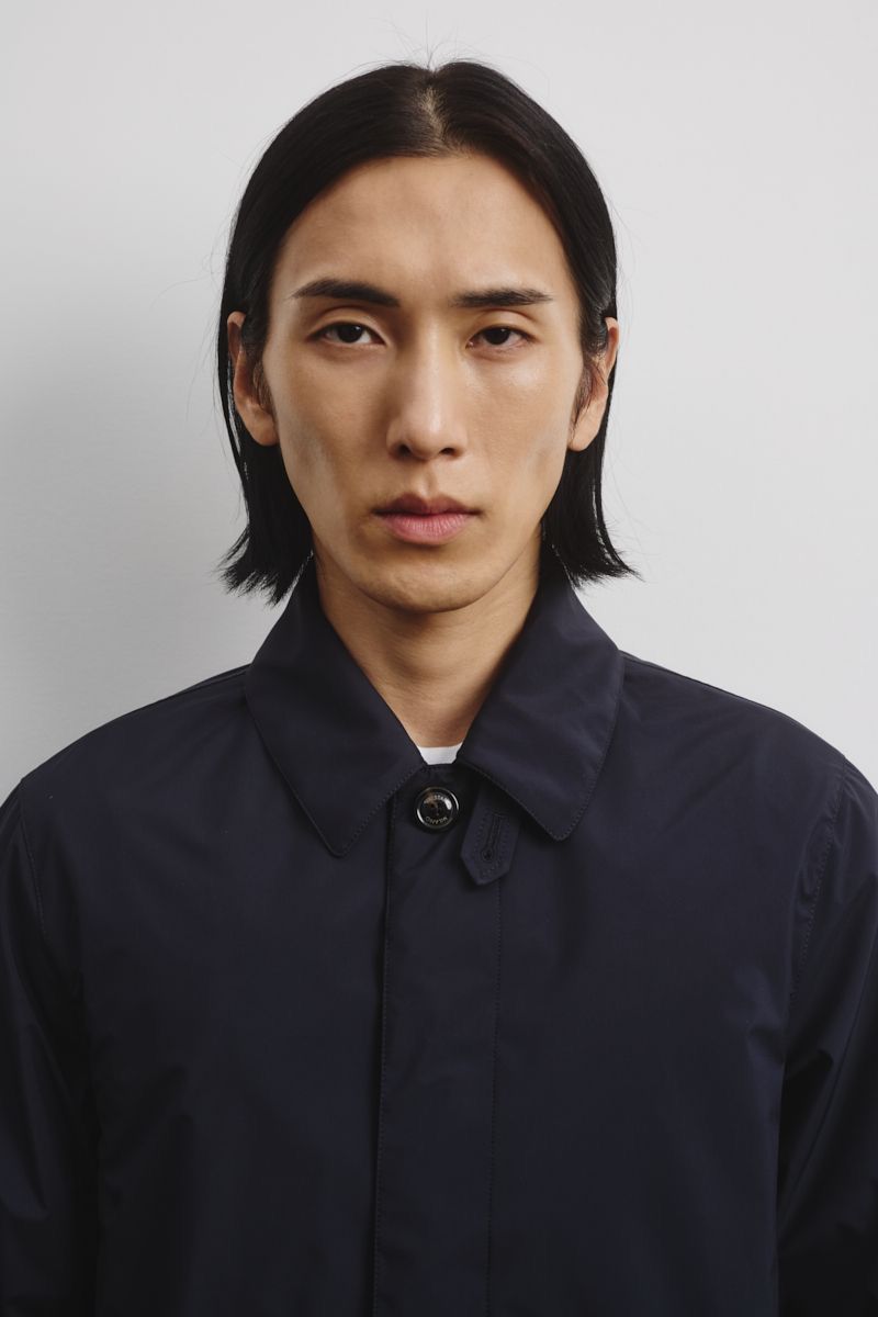Portrait of a young Asian man in a navy collared jacket against a plain white background, showcasing fashion and style.