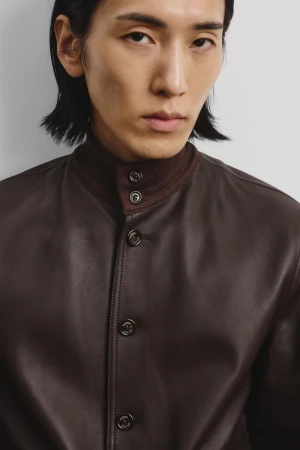 Model Hyuk Kim wearing a dark brown leather button-up jacket with a stand collar against a neutral studio backdrop.
