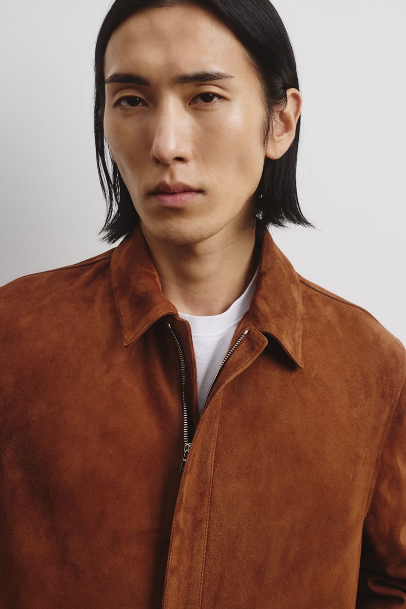 Portrait of an adult male in a brown suede jacket and white t-shirt against a neutral background in a studio setting.