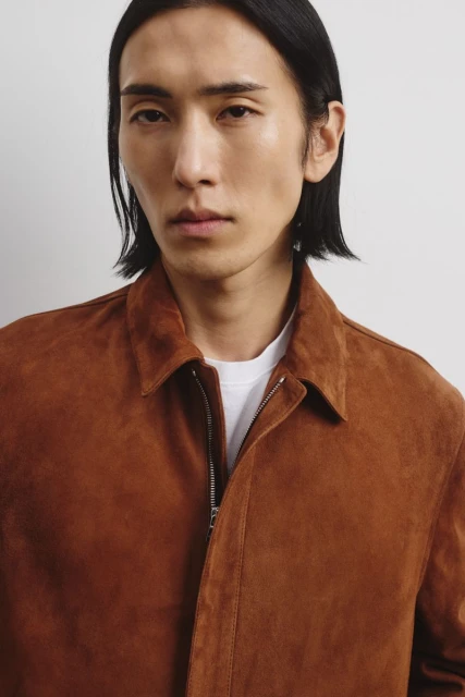 Portrait of an adult male in a brown suede jacket and white t-shirt against a neutral background in a studio setting.