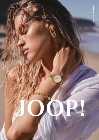 Model Kim Riekenberg wearing a gold wristwatch, chain bracelet, and earring with a white shirt on a beach.