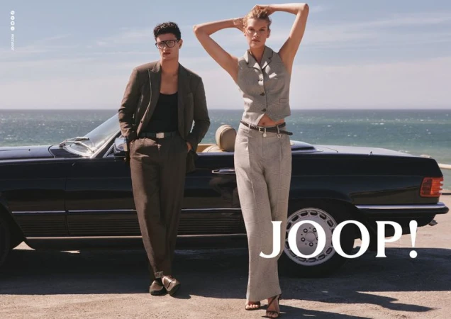 Kim Riekenberg and Gianluca Alessi in tailored suiting posing beside a black vintage convertible with the ocean in the background.