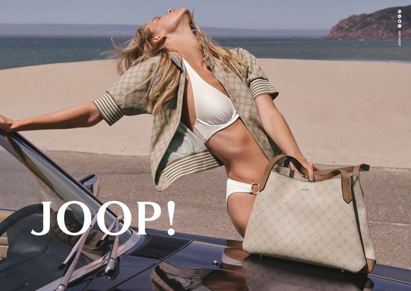 Kim Riekenberg wearing a white bikini and beige monogram jacket while leaning against a convertible on a coastal road.