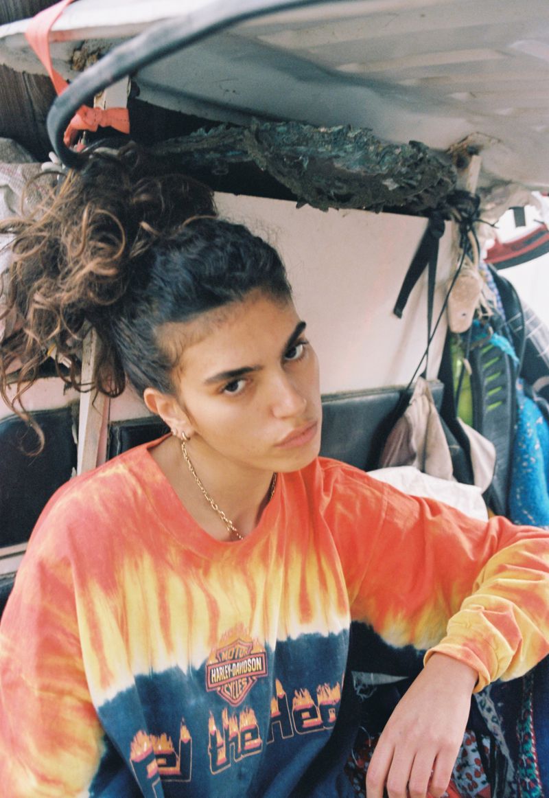 Portrait of a young adult female wearing a Harley-Davidson t-shirt with curly hair in a ponytail, posing indoors.