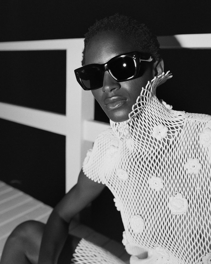 Mona Tougaard wearing black rectangular sunglasses and a white open-knit high-neck top in a high-contrast black and white portrait.