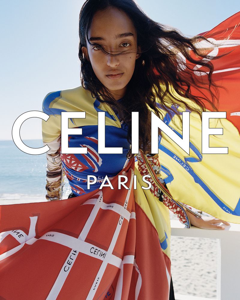 Model Mona Tougaard wearing vibrant graphic Celine silk scarves outdoors against an ocean backdrop.