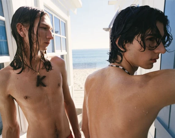 Two shirtless male models with wet dark hair standing outdoors by a beach house overlooking the ocean for Celine.